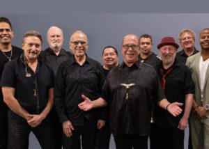 Tower of Power band members pose for a group photo, smiling and looking at the camera.
