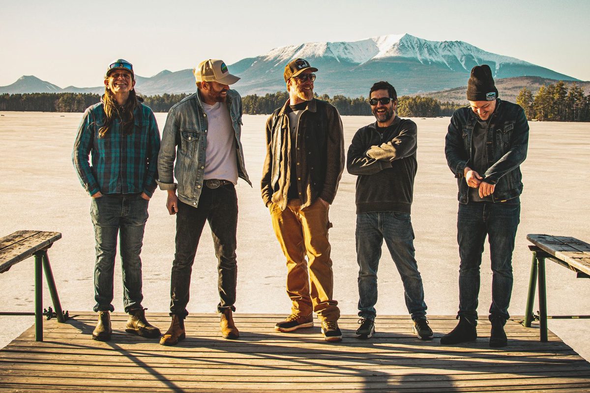 The Mallett Brothers band posing on a dock with a snowy mountain backdrop.